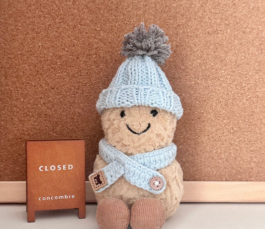 A Jellycat Amuseable plush wearing a handmade light blue knit winter set, including a pom-pom beanie and a matching scarf.