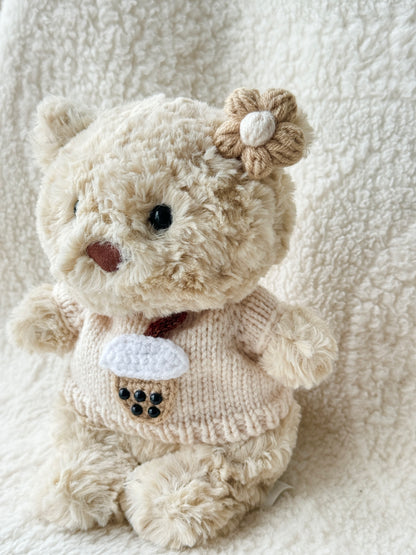 Jellycat Bartholomew Bear Junior in handmade cream knit boba sweater with tan crochet flower hair clip, angled side view