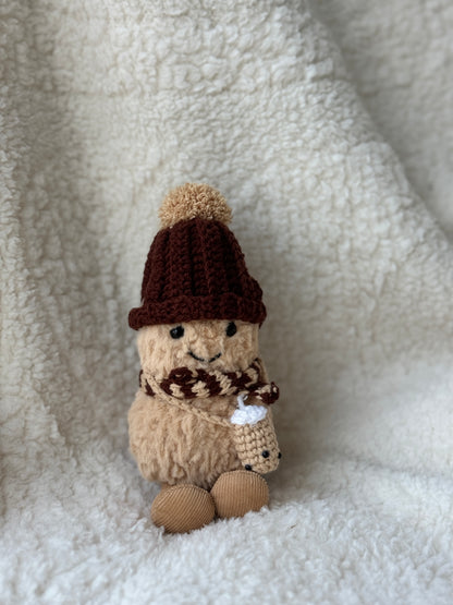 Jellycat Peanut in handmade crochet boba tea outfit — chocolate hat with caramel pom-pom, brown cream scarf, mini boba accessory, slight low-angle view on fluffy white backdrop
