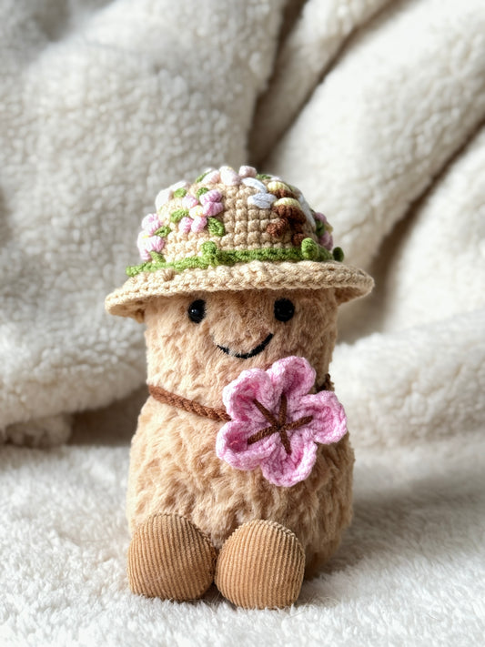 Jellycat Amuseable Peanut styled with a spring crochet hat decorated with flowers and bee, holding a crochet pink flower.