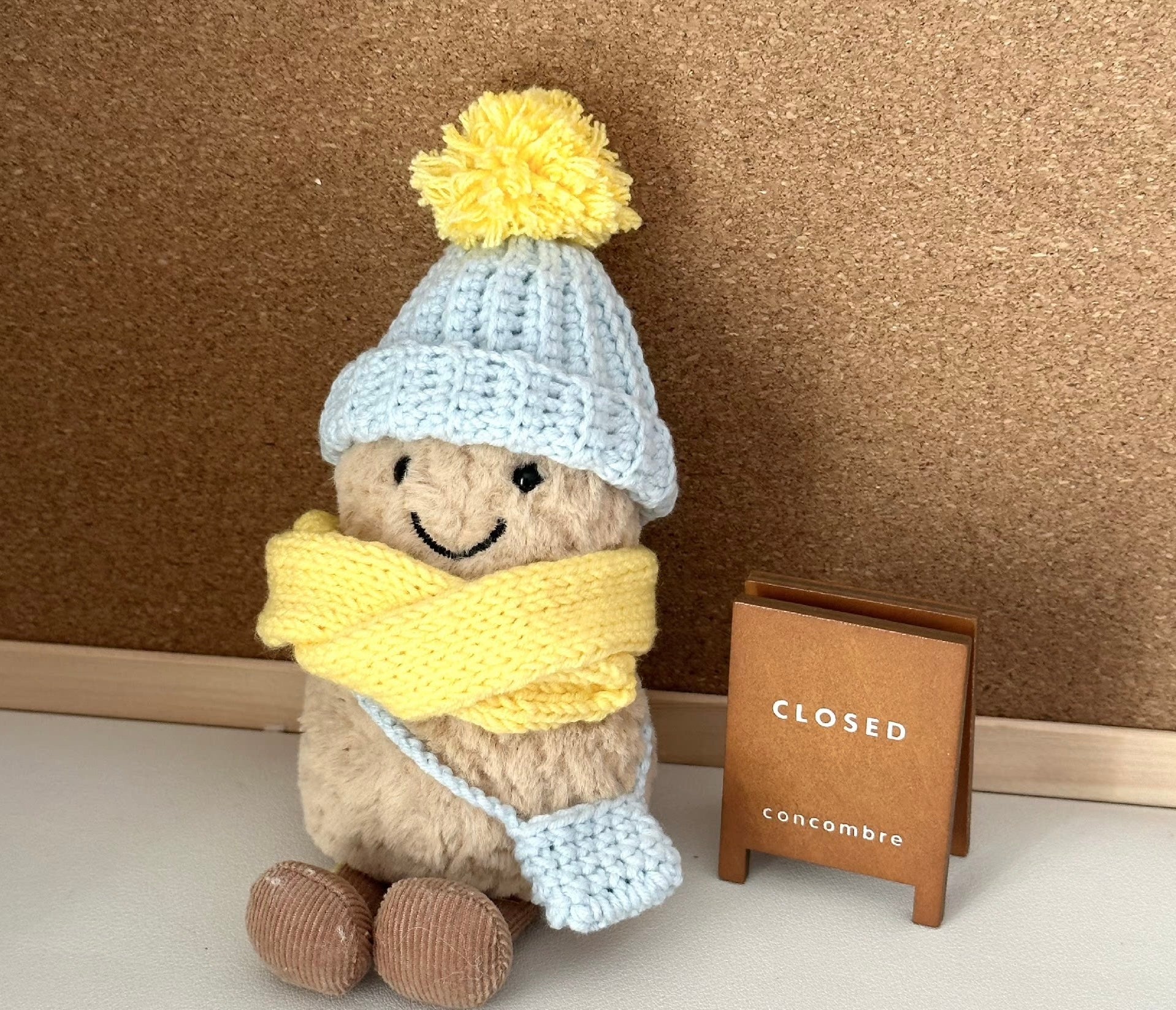 A Jellycat Amuseable plush dressed in a handmade crochet winter outfit. The light blue pom-pom beanie and matching crossbody bag pair perfectly with a vibrant yellow scarf. 