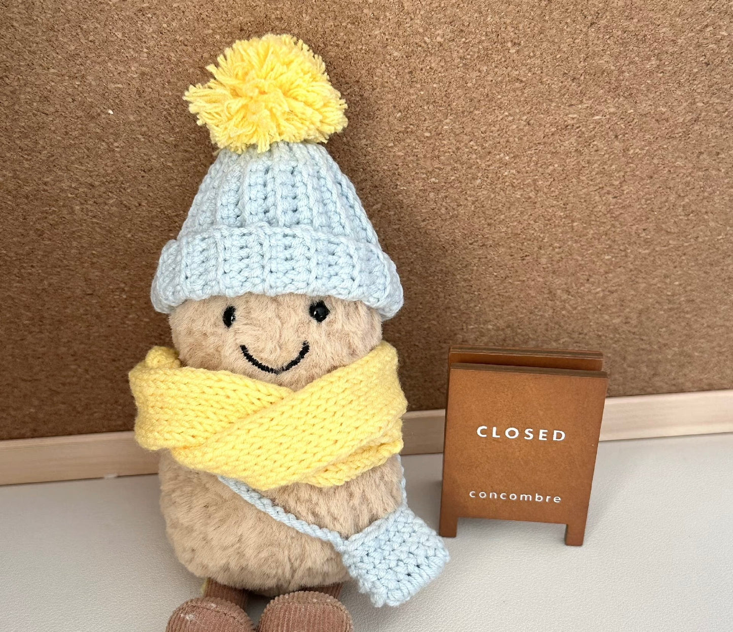 A Jellycat Amuseable plush dressed in a handmade crochet winter outfit. The light blue pom-pom beanie and matching crossbody bag pair perfectly with a vibrant yellow scarf. 