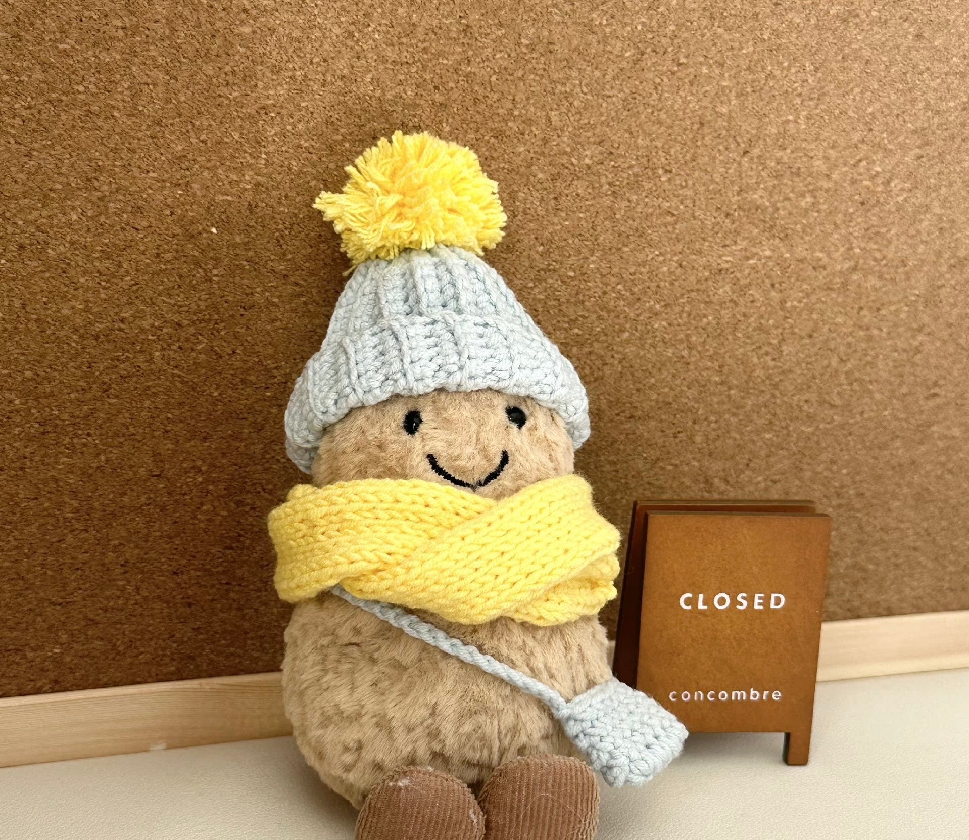 A Jellycat Amuseable plush dressed in a handmade crochet winter outfit. The light blue pom-pom beanie and matching crossbody bag pair perfectly with a vibrant yellow scarf. 