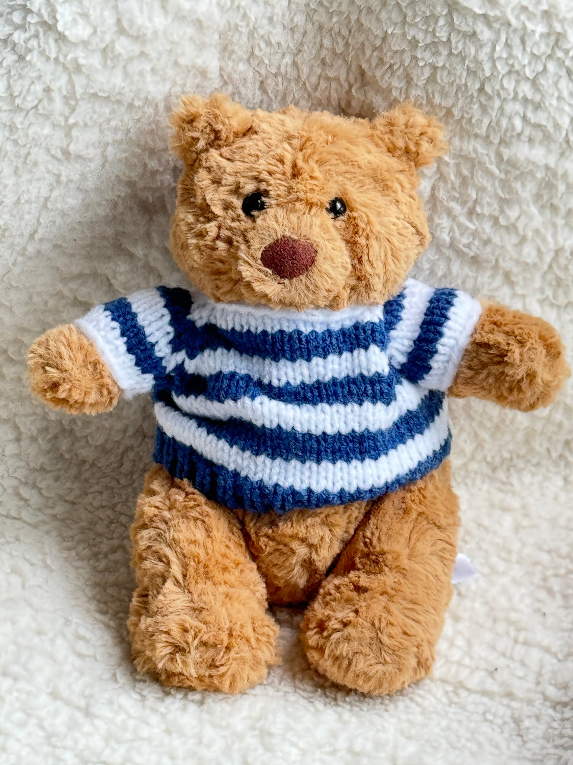 Tiny Jellycat Bartholomew Bear wearing a handmade navy blue and white striped nautical sweater, styled in a cozy soft cream fabric setting.