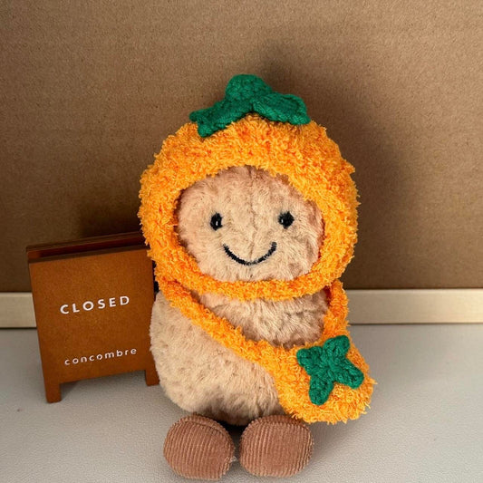 A Jellycat Amuseables plush dressed in a handmade crochet orange outfit, featuring a vibrant orange hood with a green leafy top and a matching bag.