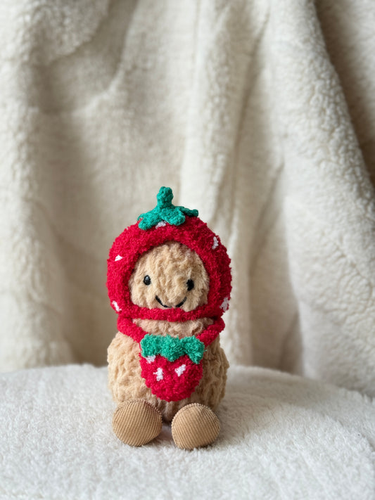Jellycat Peanut wearing a handmade crochet strawberry bonnet and matching strawberry bag on a soft cream blanket.
