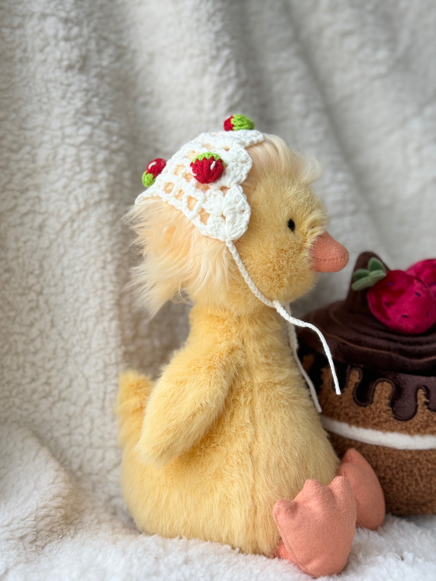 Side view of Jellycat Dorit Duck wearing a handmade crochet strawberry bonnet, a cute plush accessory with cottagecore style and soft cream crochet texture.