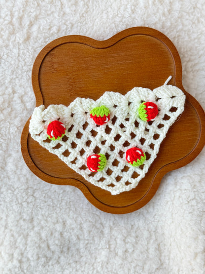 Flat lay of handmade crochet strawberry triangle bonnet on a wooden tray, showing the cream crochet mesh pattern and tiny strawberry details for Jellycat Dorit Duck.