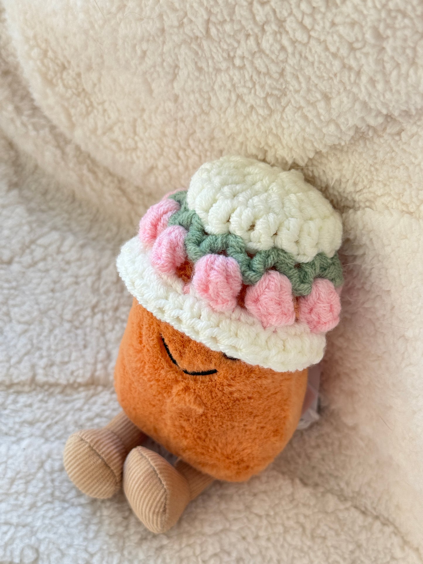 Close-up of a Jellycat Bean plush wearing a crochet floral hat with pink tulip details and soft cream yarn.